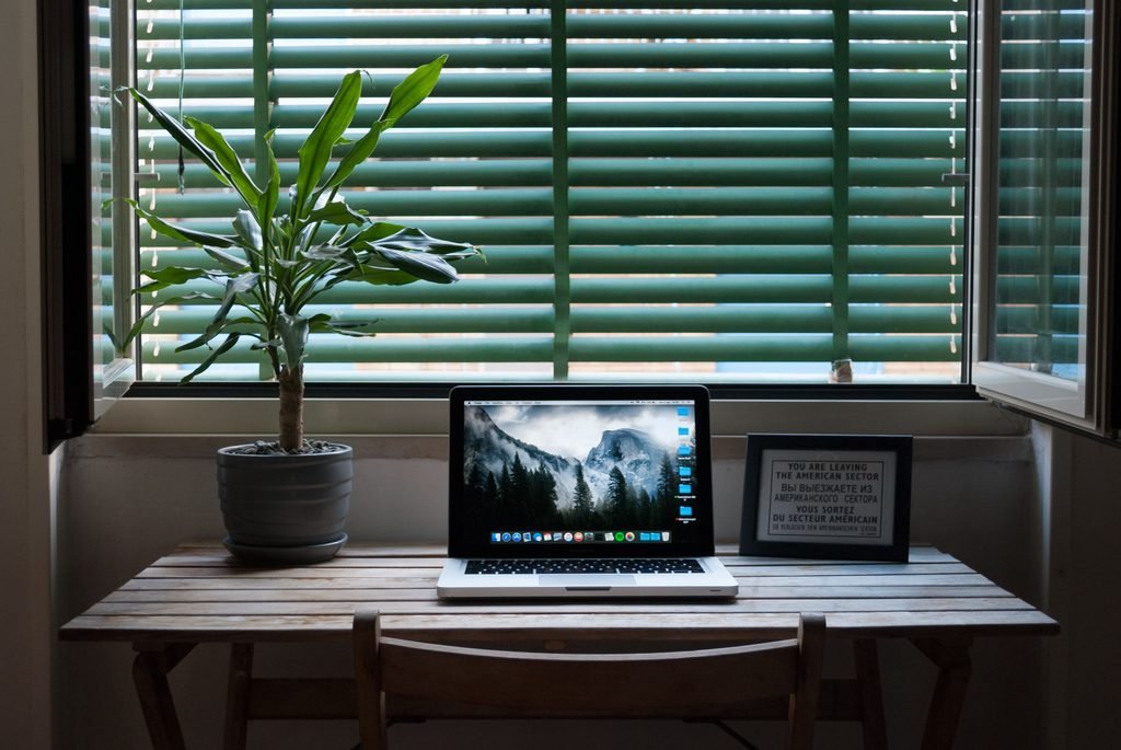 Small wooden desk setup with a laptop and indoor plant beside a window