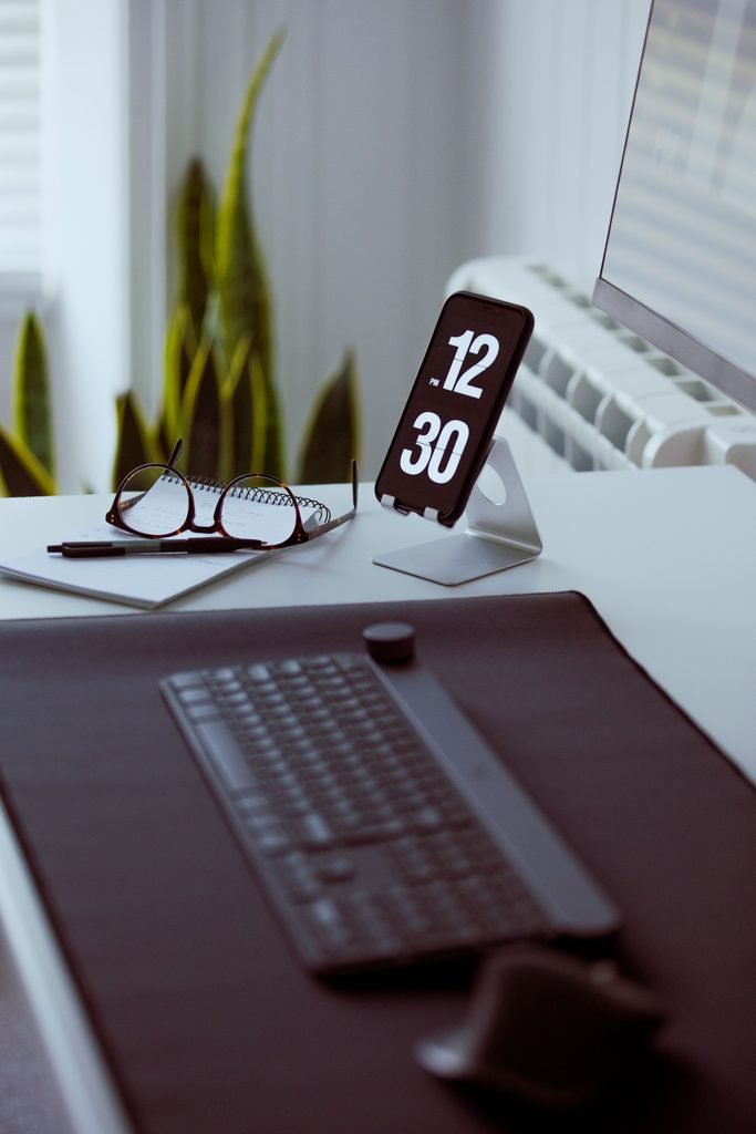 Organized desk with keyboard, smartphone stand, glasses, and notebook
