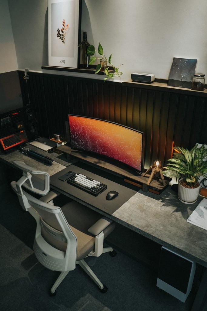 Modern desk setup with a wall shelf above a widescreen monitor and a white office chair